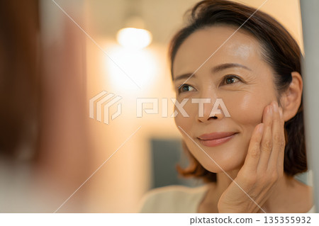 一位日本女性正在鏡子前檢查皮膚。圖片展示了護膚和美容流程。 135355932