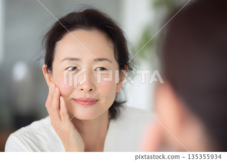 一位日本女性正在鏡子前檢查皮膚。圖片展示了護膚和美容流程。 135355934
