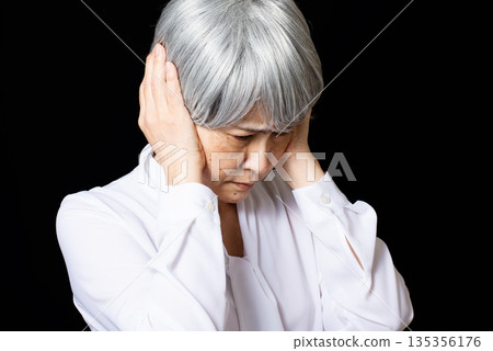 一位頭髮花白的老婦人雙手摀著耳朵。 135356176