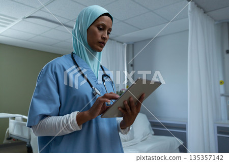 Female nurse reviewing data on tablet by bed wearing stethoscope with privacy curtains behind Female nurse reviewing data on tablet by bed wearing stethoscope with privacy curtains behind 135357142