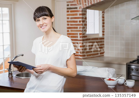 Woman holding tablet and leaning against wooden countertop in kitchen near sink and stove Woman holding tablet and leaning against wooden countertop in kitchen near sink and stove 135357149