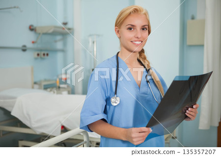 Female radiology tech wearing blue scrubs holding X-ray film in exam room, hospital bed, copy space Female radiology tech wearing blue scrubs holding X-ray film in exam room, hospital bed, copy space 135357207