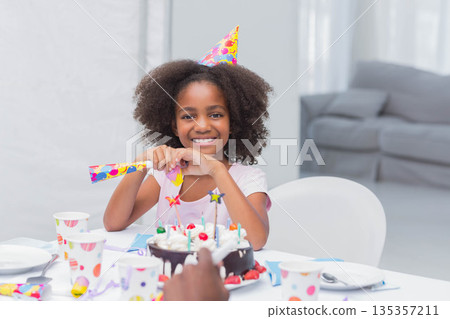 African American child smiling wearing party hat sitting at home dining table with chocolate cake 135357211