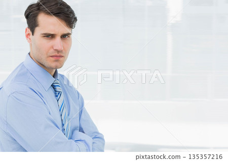 Male wearing blue shirt and striped tie, standing by blinds near windows at office, copy space Male wearing blue shirt and striped tie, standing by blinds near windows at office, copy space 135357216