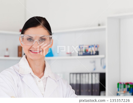 Female scientist handling test tubes in bright laboratory wearing protective goggles and lab coat 135357226