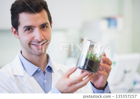 Male researcher wearing lab coat holding glass beaker with soil and sprout in lab, copy space Male researcher wearing lab coat holding glass beaker with soil and sprout in lab, copy space 135357257