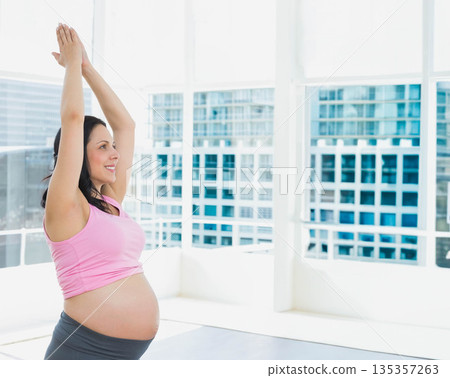 Pregnant woman practicing yoga stretch on mat in fitness studio with glass windows, copy space 135357263