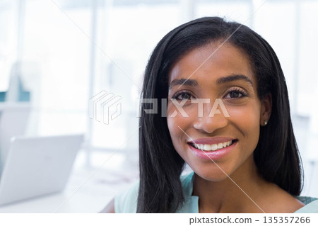 African American woman smiling while typing on silver laptop at desk in modern office, copy space 135357266