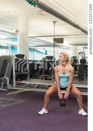 Female exerciser performing kettlebell squat on purple rubber floor in fitness center Female exerciser performing kettlebell squat on purple rubber floor in fitness center 135357269