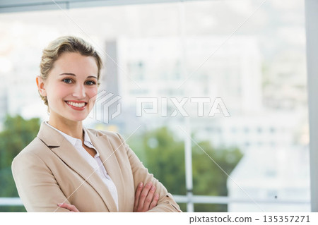 Businesswoman in blazer smiling and standing near glass window in office with city view, copy space Businesswoman in blazer smiling and standing near glass window in office with city view, copy space 135357271