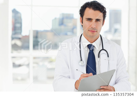 Mid adult doctor wearing stethoscope noting clipboard with pen at clinic window skyline, copy space 135357304