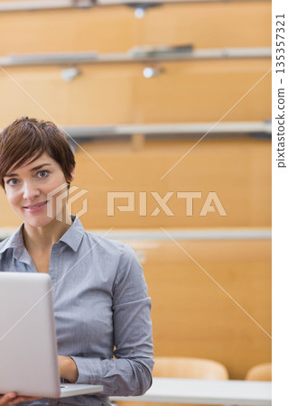 Woman working on laptop at desk in lecture hall with wooden benches and railings, copy space 135357321