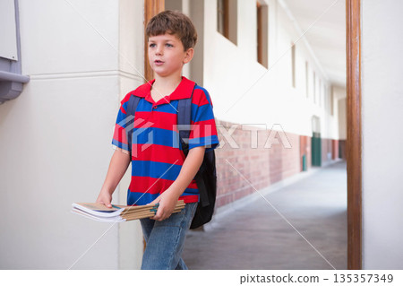 Boy student walking through school corridor holding stack of notebooks and folders, copy space Boy student walking through school corridor holding stack of notebooks and folders, copy space 135357349