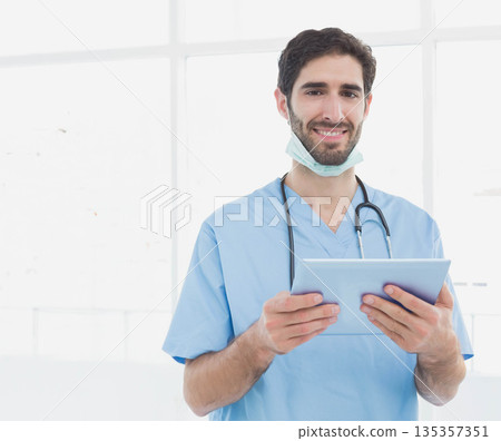 Adult medic in scrubs using tablet in clinic wearing stethoscope and mask under chin, copy space Adult medic in scrubs using tablet in clinic wearing stethoscope and mask under chin, copy space 135357351