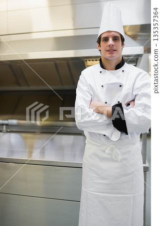 Male chef posing with arms crossed at cooking station under stainless steel range hood copy space Male chef posing with arms crossed at cooking station under stainless steel range hood copy space 135357364
