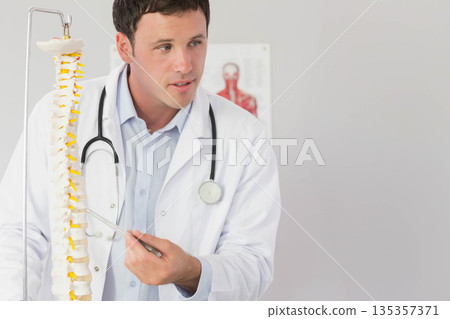 Male doctor pointing at lumbar spine model with metal pointer in exam room wearing stethoscope Male doctor pointing at lumbar spine model with metal pointer in exam room wearing stethoscope 135357371