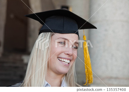 Woman smiling and celebrating graduation while wearing mortarboard cap under arched entrance Woman smiling and celebrating graduation while wearing mortarboard cap under arched entrance 135357408