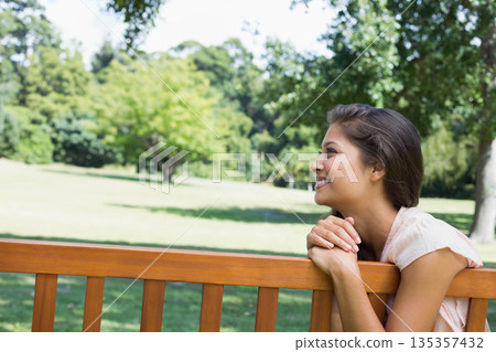 Woman leaning forearms on wooden park bench in city park with grass and trees, copy space Woman leaning forearms on wooden park bench in city park with grass and trees, copy space 135357432