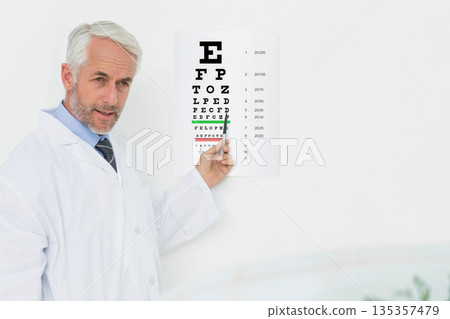 Senior male optometrist holding pointer and pointing at Snellen eye chart in exam room, copy space 135357479