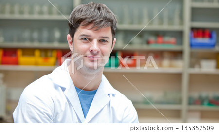 Man wearing white lab coat standing in laboratory among metal shelves with colored bins, glassware Man wearing white lab coat standing in laboratory among metal shelves with colored bins, glassware 135357509