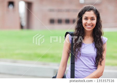 Hispanic student standing on campus path right side holding black bag strap and smiling, copy space Hispanic student standing on campus path right side holding black bag strap and smiling, copy space 135357516