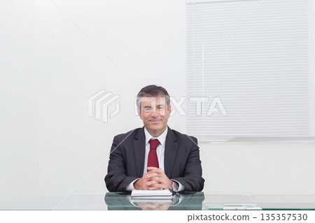 Senior man placing hands wearing wristwatch on closed notebook at transparent glass desk in office 135357530