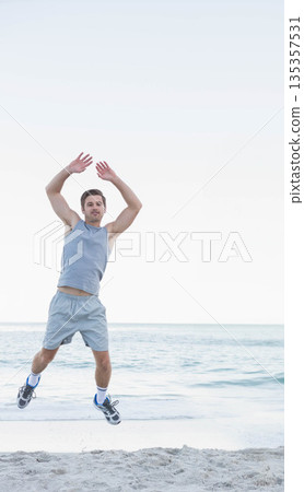 Man leaping on sandy beach wearing sportswear and running shoes with calm ocean backdrop Man leaping on sandy beach wearing sportswear and running shoes with calm ocean backdrop 135357531