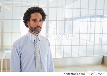 African American man standing in bright office in light blue shirt, patterned tie by grid windows 135357548
