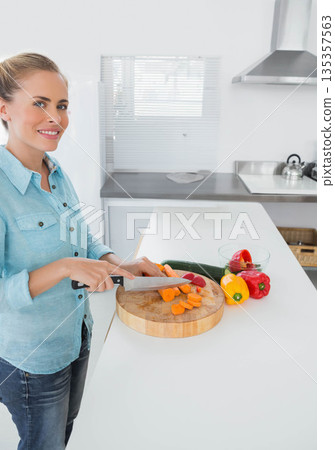 Woman slicing carrots on cutting board at kitchen counter with peppers, zucchini, copy space 135357563