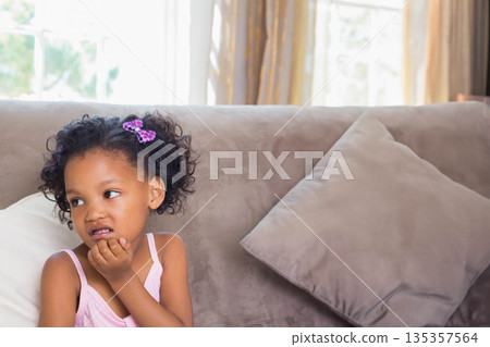 Preschool-aged African American girl sitting on couch resting chin by window, copy space 135357564
