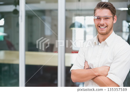 Man wearing smart glasses and shirt standing in office beside glass partition and table, copy space 135357589