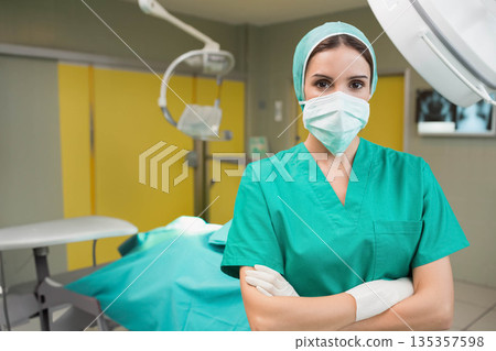 Female surgeon folding arms in operating room with table, surgical lamp, x-ray display, copy space Female surgeon folding arms in operating room with table, surgical lamp, x-ray display, copy space 135357598