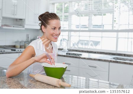 Woman in her thirties whisking ingredients in green bowl on granite countertop in home kitchen Woman in her thirties whisking ingredients in green bowl on granite countertop in home kitchen 135357612