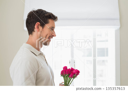 Man standing in softly lit home holding vibrant pink rose bouquet near window, copy space Man standing in softly lit home holding vibrant pink rose bouquet near window, copy space 135357613