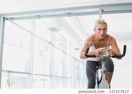 Female athlete riding stationary bike in fitness studio wearing sportswear with console, copy space 135357617