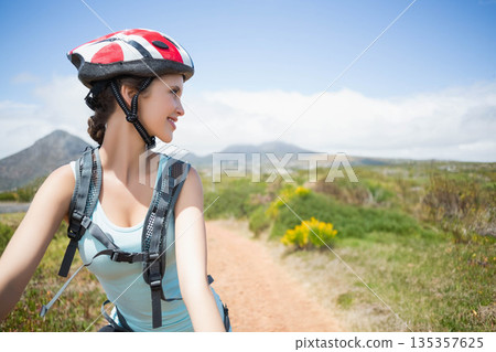 Female cyclist smiling while glancing left on dirt trail with helmet and hydration pack, copy space 135357625