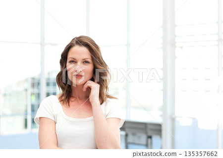 Woman standing in bright modern studio facing grid-style windows wearing white T-shirt Woman standing in bright modern studio facing grid-style windows wearing white T-shirt 135357662