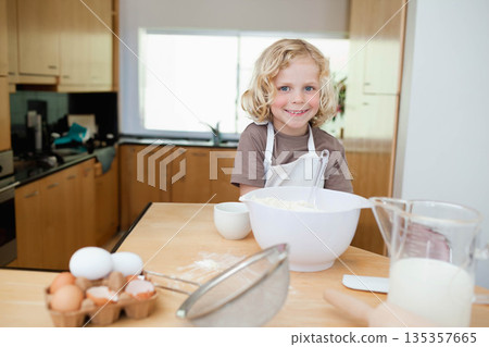 Boy wearing white apron mixing ingredients at kitchen counter with mixing bowl and eggs carton Boy wearing white apron mixing ingredients at kitchen counter with mixing bowl and eggs carton 135357665