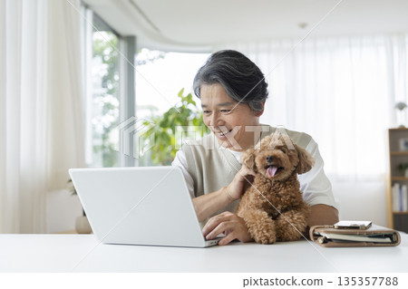 A man in his 50s working on a laptop while holding his pet dog A man in his 50s working on a laptop while holding his pet dog 135357788
