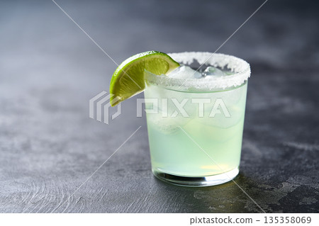 Margarita cocktail with ice cubes in glass and lime on a black table with copy space for text. Margarita cocktail with ice cubes in glass and lime on a black table with copy space for text. 135358069