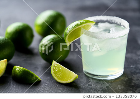 Classic lime margarita cocktail with sliced and whole limes sitting on a black table. Classic lime margarita cocktail with sliced and whole limes sitting on a black table. 135358070