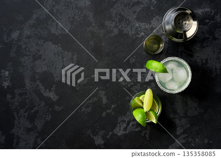 Margarita cocktail with ice cubes in glass and lime on a black table , top view. Margarita cocktail with ice cubes in glass and lime on a black table , top view. 135358085