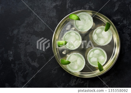 metal tray with traditional cocktail Margarita served in salt rimmed tumbler over ice and garnished with a lime.Top view. 135358092