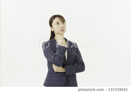 A young Japanese woman in a suit with her hand on her chin and worried about something on a white background A young Japanese woman in a suit with her hand on her chin and worried about something on a white background 135358681