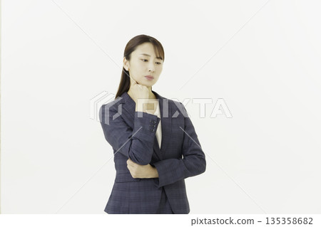 一位年輕的日本女子身穿西裝,手托下巴,在白色背景下顯得憂慮。 一位年輕的日本女子身穿西裝,手托下巴,在白色背景下顯得憂慮。 135358682