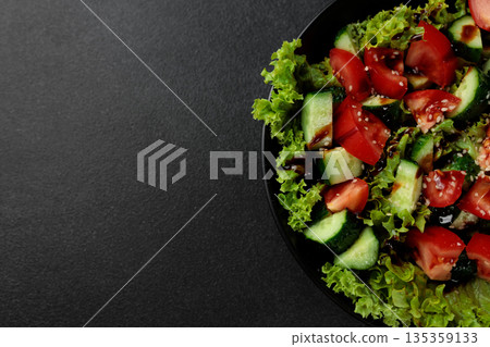 Vegetable salad of tomatoes, cucumbers, onions, lettuce dressed with aromatic dressing in a black plate on a gray background Vegetable salad of tomatoes, cucumbers, onions, lettuce dressed with aromatic dressing in a black plate on a gray background 135359133