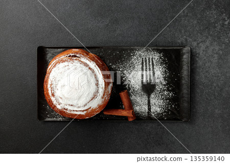 Round, delicious bun with cinnamon and powdered sugar on a black plate on a gray background Round, delicious bun with cinnamon and powdered sugar on a black plate on a gray background 135359140