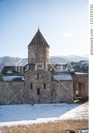 Stone church of the Tatev monastery stands against snowy mountains under clear winter sky, gray masonry, sharp light, calm and timeless mood 135359192