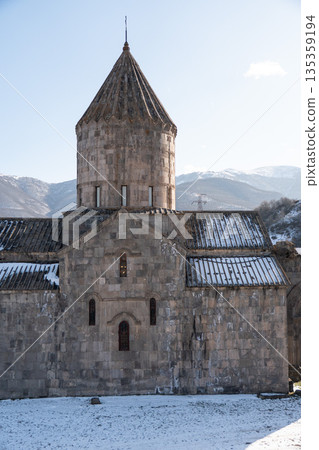 Stone church of the Tatev monastery stands against snowy mountains under clear winter sky, gray masonry, sharp light, calm and timeless mood Stone church of the Tatev monastery stands against snowy mountains under clear winter sky, gray masonry, sharp light, calm and timeless mood 135359194