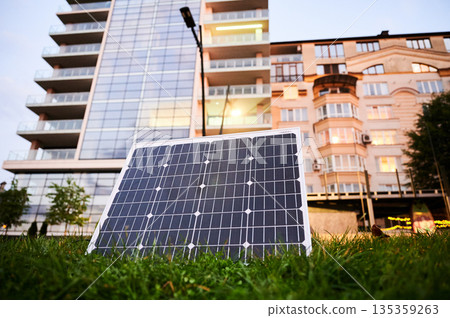 Photovoltaic solar panel in front of modern apartment building with balconies, suggesting residential or mixed-use. Concept of integration of sustainable renewable energy sources into architecture. 135359263